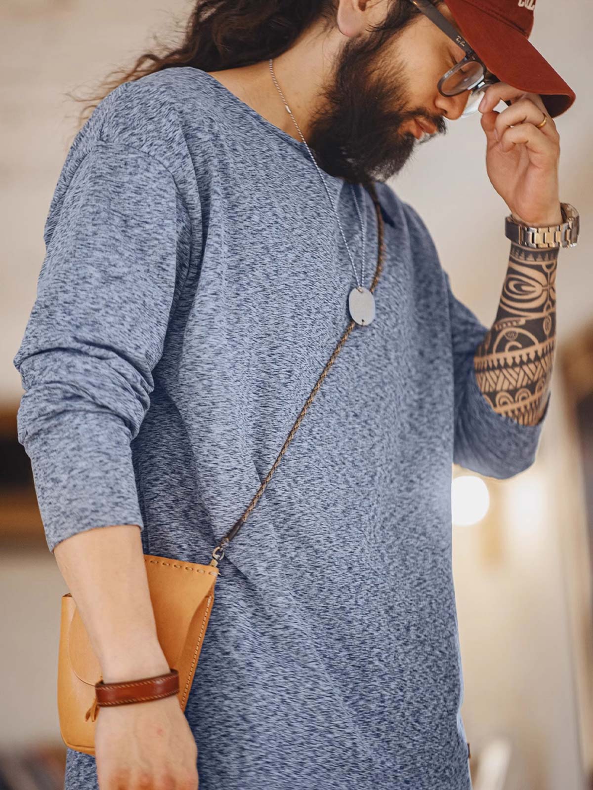 詳細画像: カチオン糸による独特な風合いとヴィンテージ感漂うブラウンのレザーパッチのディテールをクローズアップした画像。見た目の個性と高級感を強調。
モデル画像: 両面フリース起毛 長袖Tシャツを着用したモデルが、リラックスしたカジュアルコーディネートを披露。インナーとしても単独でも活躍するアイテム。