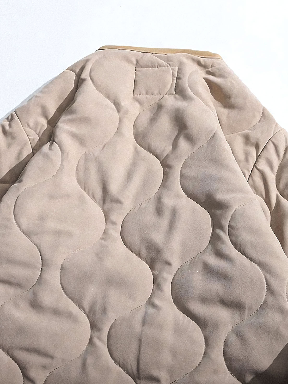 製品画像
ピーチスキン ノーカラー キルティング 中綿ジャケット全体図。滑らかなピーチスキン素材と波形キルティングが特徴の軽量ユニセックスアウター。
詳細画像
柔らかなピーチスキン素材の質感、立体感を生む波形キルティングステッチ、軽量ウォッシュドコットン中綿のディテール特写。