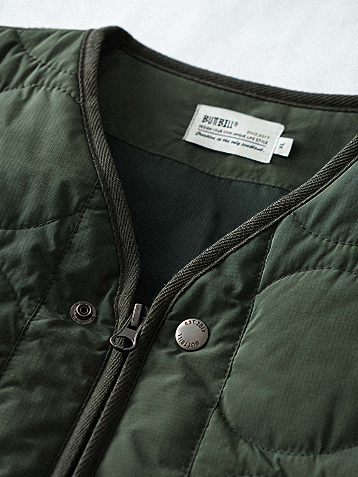 製品画像
「テフロン加工 三防テクノロジー ダイヤキルティング中綿ジャケット全体像。防水、防油、防汚の三防機能と3M™シンサレート中綿が特徴で、軽量で暖かい冬のアウター」
詳細画像
「テフロン加工 ダイヤキルティング中綿ジャケットのダブルジッパーとスナップボタンのディテールクローズアップ。防風性とデザイン性を両立」