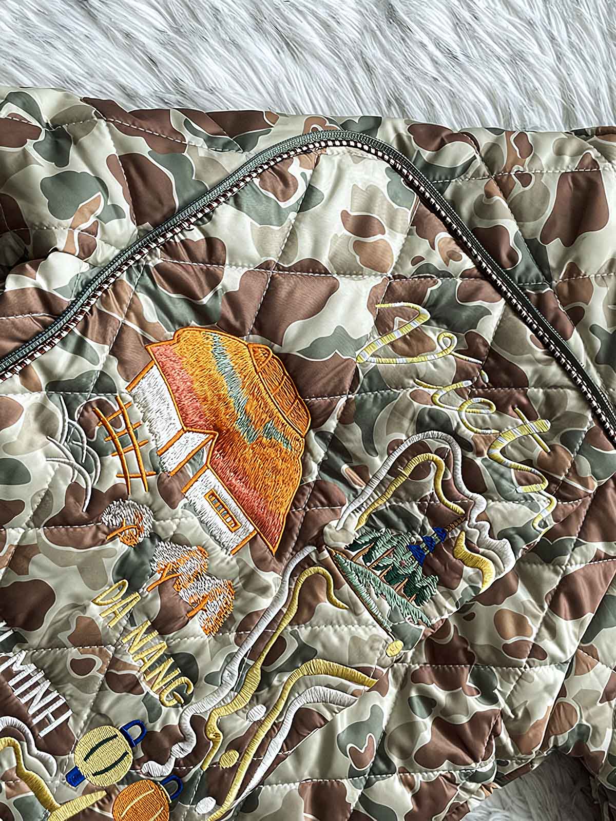 製品画像
「カモフラージュ刺繍ベースボールジャケット全体像。迷彩柄と平和を象徴する刺繍デザインが特徴のレトロスタイルジャケット」
詳細画像
「カモフラージュ刺繍ベースボールジャケットの袖部分の刺繍ディテールとストライプリブ仕様ポケットのクローズアップ。デザイン性と実用性を両立」