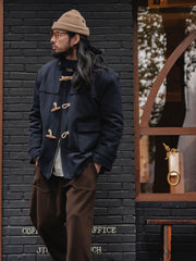 詳細画像
WWI時代のデザインを反映した木製トグルボタンと取り外し可能なストームフラップのディテール。160gウォッシャブルコットン中綿が暖かさと快適さを提供。
モデル画像
モデルがウール混ロング丈フード付きダッフルコートを着用し、冬のヴィンテージ通勤スタイルを演出。クラシックなデザインと現代的な機能性を融合した冬の必須アイテム。