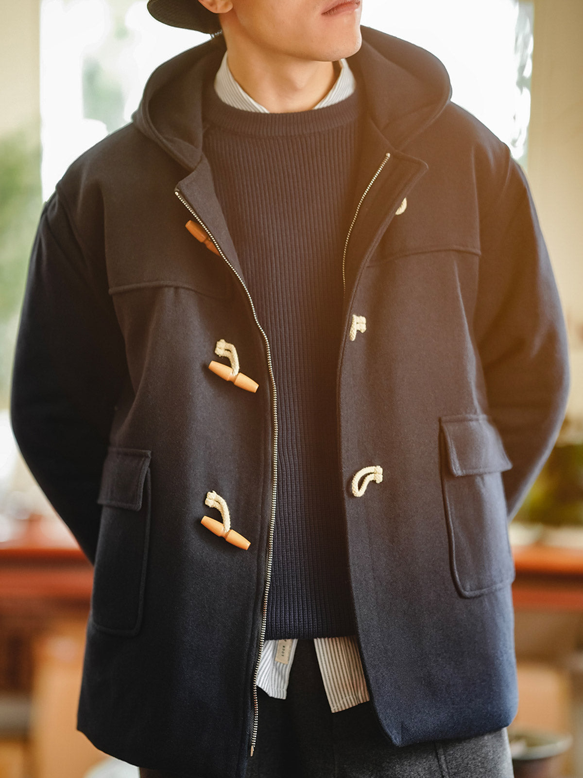 詳細画像
WWI時代のデザインを反映した木製トグルボタンと取り外し可能なストームフラップのディテール。160gウォッシャブルコットン中綿が暖かさと快適さを提供。
モデル画像
モデルがウール混ロング丈フード付きダッフルコートを着用し、冬のヴィンテージ通勤スタイルを演出。クラシックなデザインと現代的な機能性を融合した冬の必須アイテム。