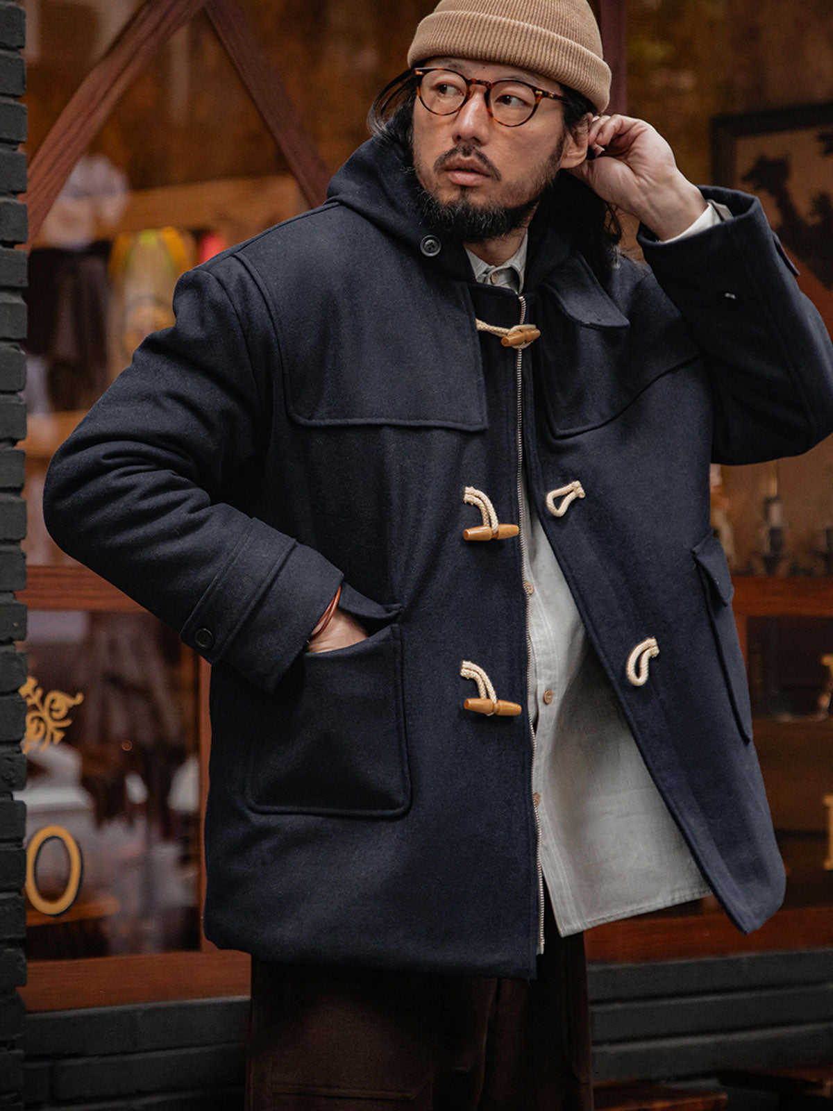 詳細画像
WWI時代のデザインを反映した木製トグルボタンと取り外し可能なストームフラップのディテール。160gウォッシャブルコットン中綿が暖かさと快適さを提供。
モデル画像
モデルがウール混ロング丈フード付きダッフルコートを着用し、冬のヴィンテージ通勤スタイルを演出。クラシックなデザインと現代的な機能性を融合した冬の必須アイテム。