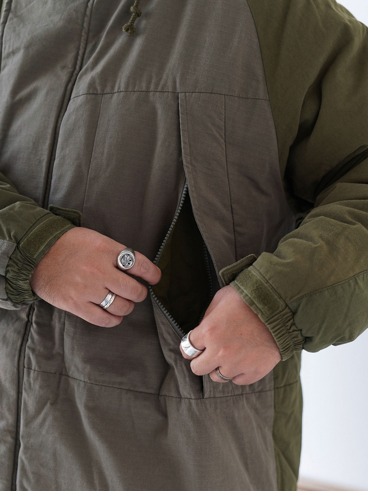 詳細画像
「ペイズリー柄の裏地と日本製YKK製の両開きファスナーのディテールを特写した画像。ヴィンテージデザインと高機能性を兼ね備えたジャケット。」
モデル画像
「モデルがトーンオントーン パッチワーク ミドル丈中綿ジャケットを着用し、デニムパンツと合わせた冬のアウトドアカジュアルスタイルを披露。」