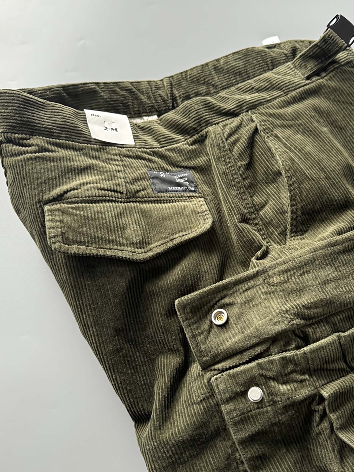 製品画像
「重厚なコーデュロイ素材を使用したカーゴパンツの全体展示図。クラシックなヴィンテージスタイルと快適な履き心地を兼ね備え、テーパードシルエットが脚のラインを美しく見せるデザイン。」
詳細画像
「カーゴパンツの斜め立体ポケットのディテール特写。収納性を高めるだけでなく、全体にカーゴスタイルの立体感を加えたデザイン。」