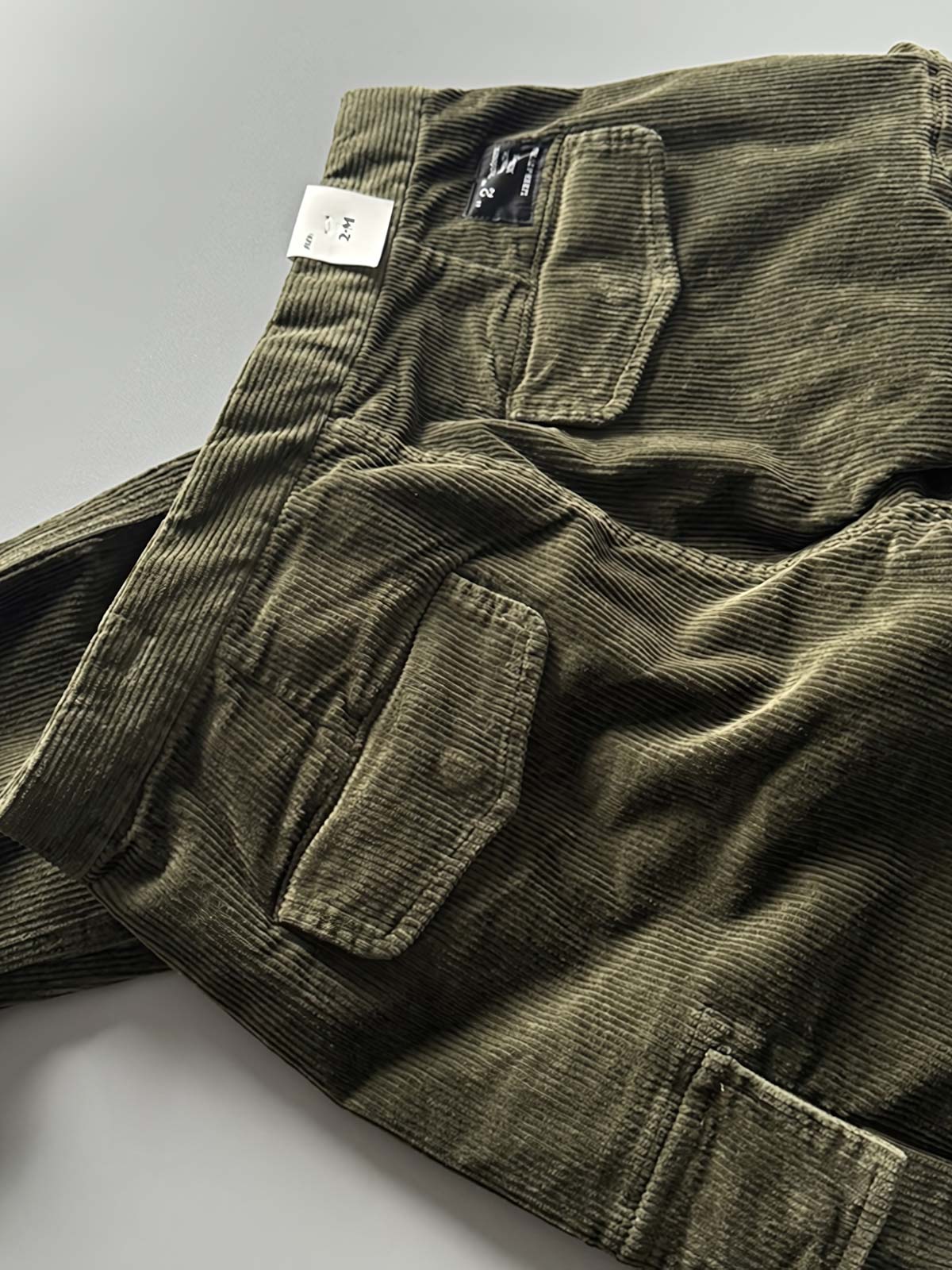 製品画像
「重厚なコーデュロイ素材を使用したカーゴパンツの全体展示図。クラシックなヴィンテージスタイルと快適な履き心地を兼ね備え、テーパードシルエットが脚のラインを美しく見せるデザイン。」
詳細画像
「カーゴパンツの斜め立体ポケットのディテール特写。収納性を高めるだけでなく、全体にカーゴスタイルの立体感を加えたデザイン。」