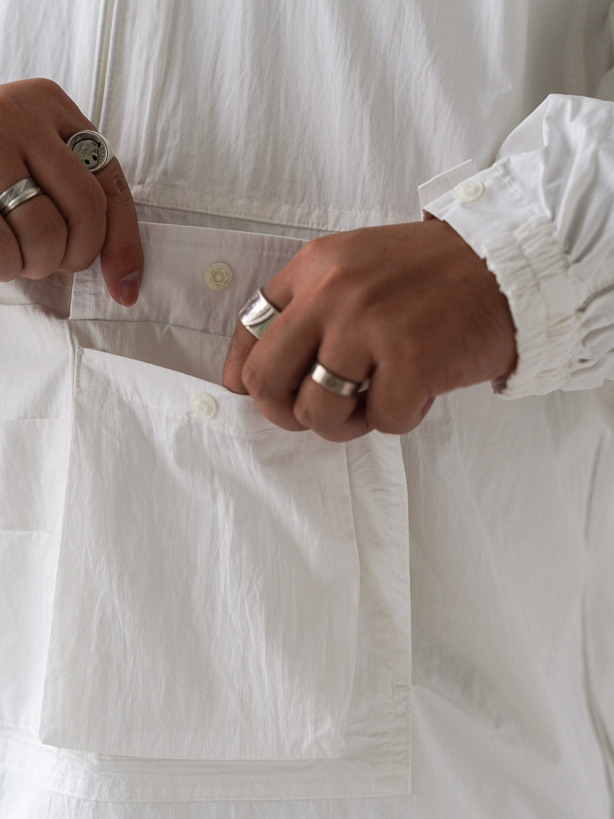 詳細画像
胸元や肩部分に施された立体的なラインデザイン、繊細なグリッド模様、そしてYKK製のマット仕上げファスナーを搭載したポケットの特写。機能性とデザイン性を両立したミリタリースタイルが際立つディテール。
モデル画像
オーバーサイズのシルエットでレイヤードスタイルを楽しめる、多ポケットジャケットを着用したモデルのアウトドアコーディネート。タウンユースやキャンプシーンでの汎用性の高さが映えるスタイル。