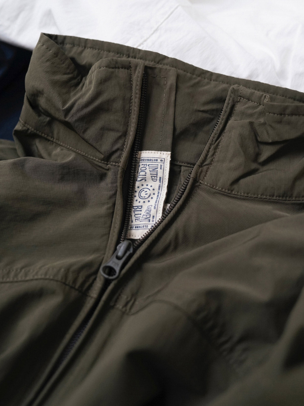 製品画像
軽量で耐久性に優れたナイロンとポリエステルの混紡素材を使用した、多ポケットハーフジップジャケットの全体展示。ヴィンテージ感あふれるデザインと実用的な収納性を備え、アウトドアや日常使いに最適なスタイリッシュなアイテム。
詳細画像
胸元や肩部分に施された立体的なラインデザイン、繊細なグリッド模様、そしてYKK製のマット仕上げファスナーを搭載したポケットの特写。機能性とデザイン性を両立したミリタリースタイルが際立つディテール。