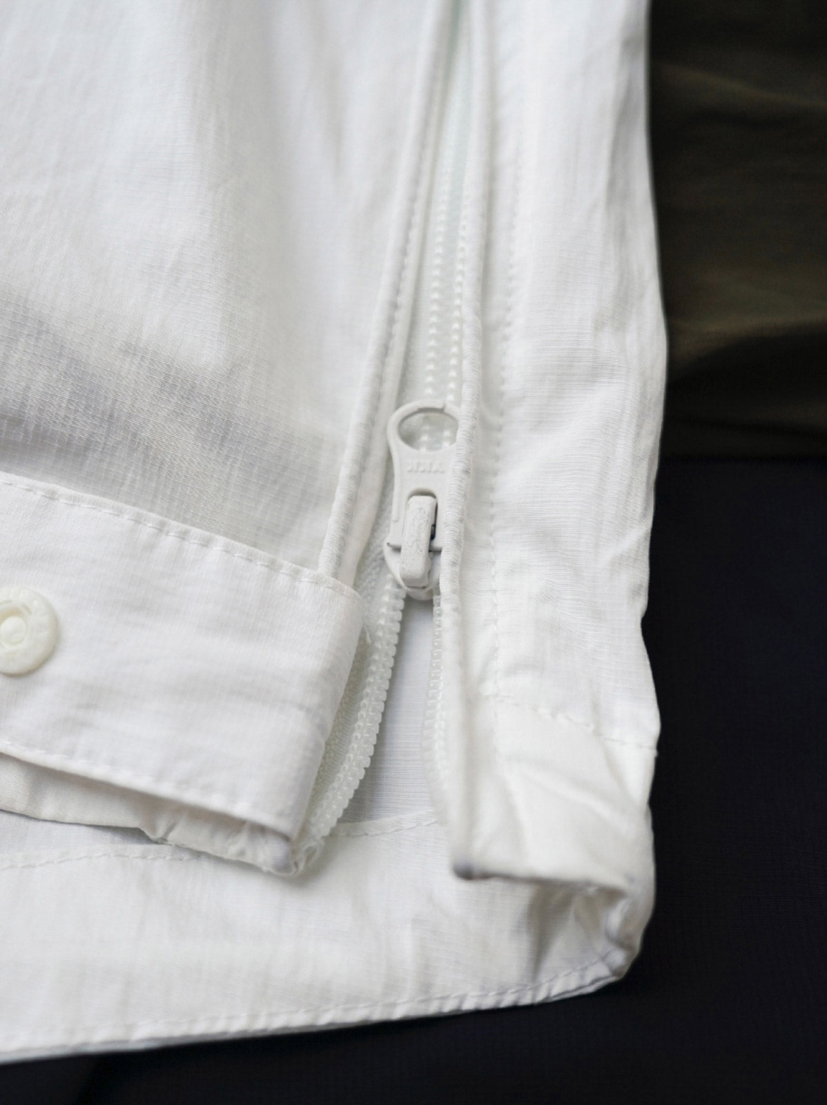 製品画像
軽量で耐久性に優れたナイロンとポリエステルの混紡素材を使用した、多ポケットハーフジップジャケットの全体展示。ヴィンテージ感あふれるデザインと実用的な収納性を備え、アウトドアや日常使いに最適なスタイリッシュなアイテム。
詳細画像
胸元や肩部分に施された立体的なラインデザイン、繊細なグリッド模様、そしてYKK製のマット仕上げファスナーを搭載したポケットの特写。機能性とデザイン性を両立したミリタリースタイルが際立つディテール。