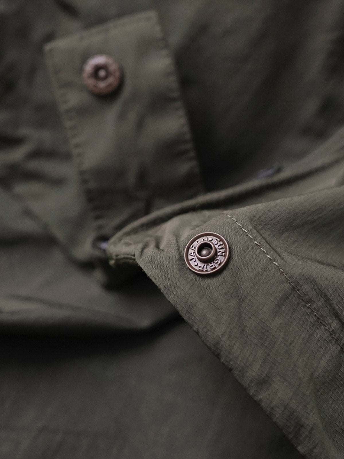 製品画像
軽量で耐久性に優れたナイロンとポリエステルの混紡素材を使用した、多ポケットハーフジップジャケットの全体展示。ヴィンテージ感あふれるデザインと実用的な収納性を備え、アウトドアや日常使いに最適なスタイリッシュなアイテム。
詳細画像
胸元や肩部分に施された立体的なラインデザイン、繊細なグリッド模様、そしてYKK製のマット仕上げファスナーを搭載したポケットの特写。機能性とデザイン性を両立したミリタリースタイルが際立つディテール。