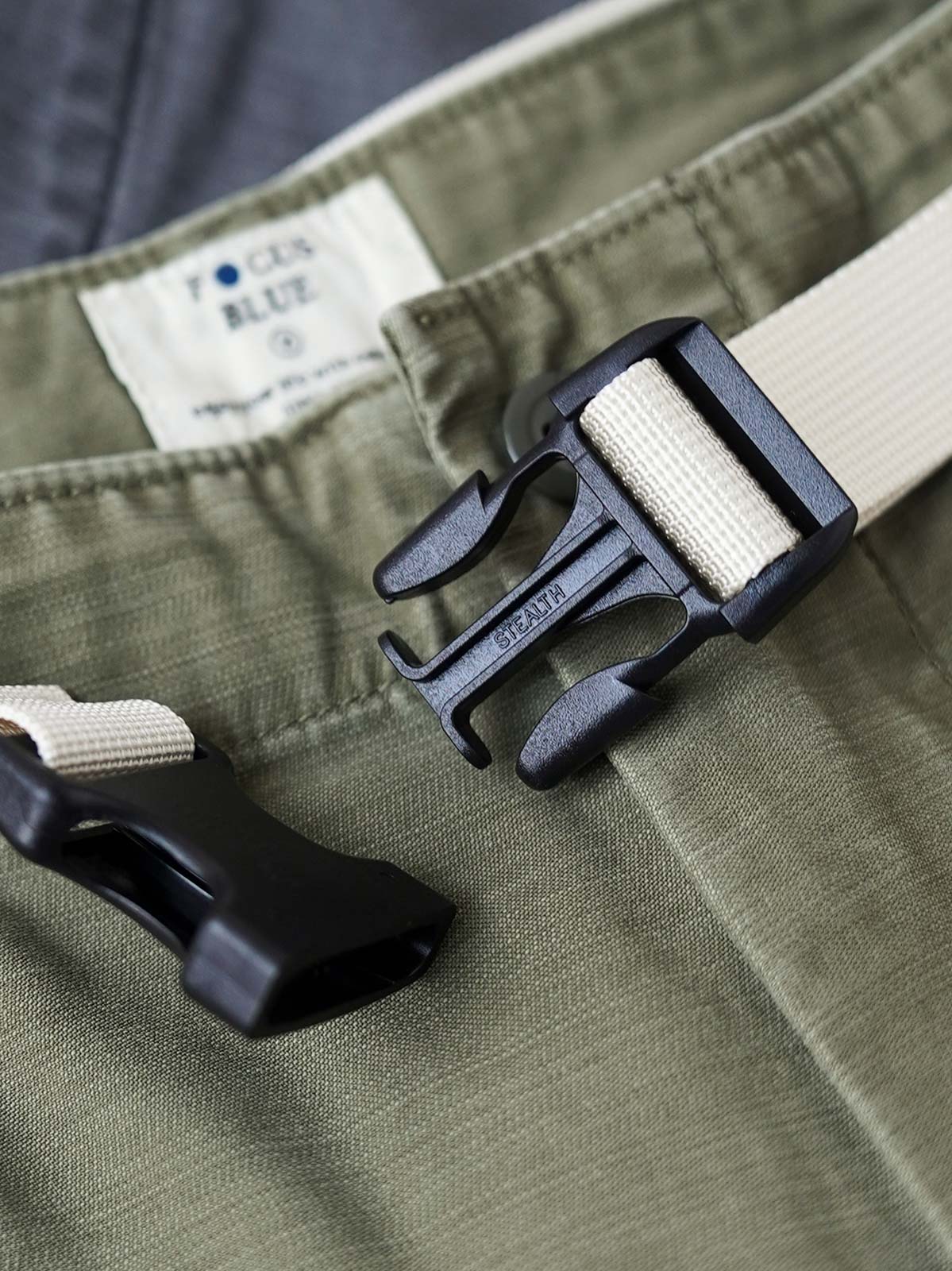 製品画像
ヴィンテージ感漂うバティック染めが特徴の多ポケットロングパンツ全体画像。ミリタリーテイストを取り入れ、300gのコットンサテン生地で耐久性と実用性を兼ね備えたデザイン。
詳細画像
バティック染めによる独特なテクスチャーや、取り外し可能なナイロンベルト、UTX Duraflexバックル、そして膝部分の補強パッチとYKK製カスタムジッパーのディテールショット。高い機能性が際立つ細部。