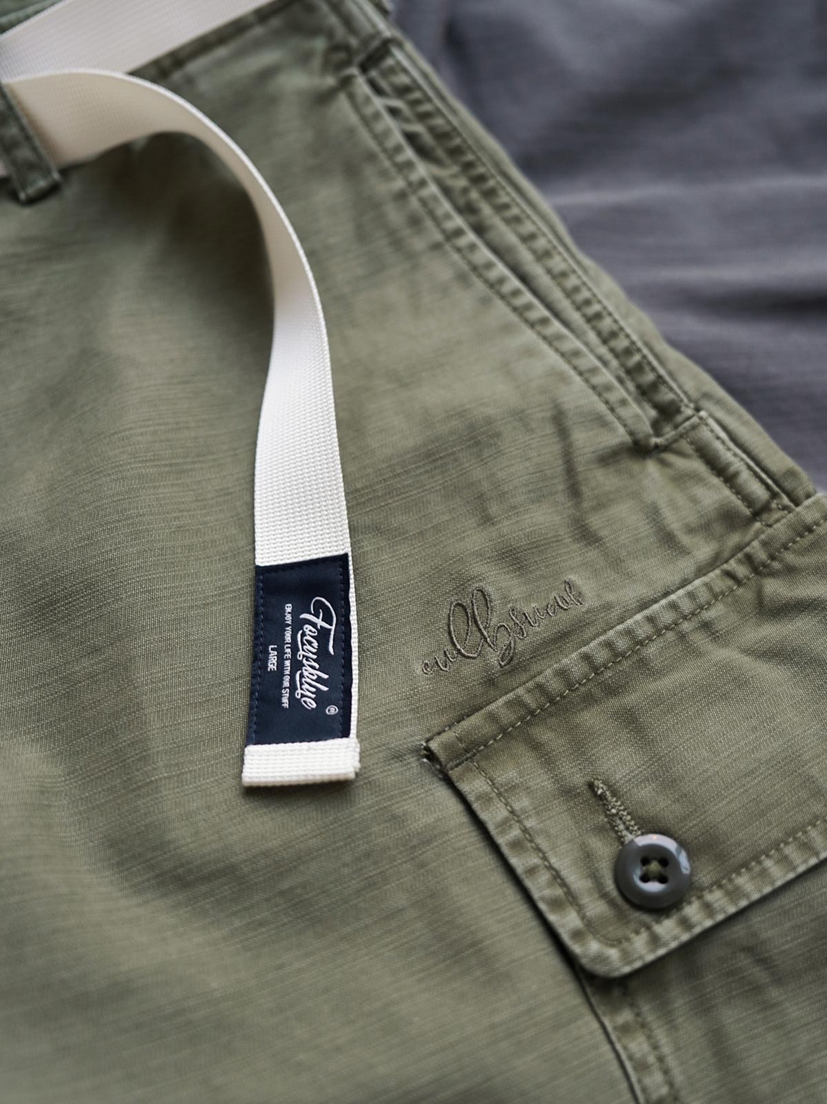 製品画像
ヴィンテージ感漂うバティック染めが特徴の多ポケットロングパンツ全体画像。ミリタリーテイストを取り入れ、300gのコットンサテン生地で耐久性と実用性を兼ね備えたデザイン。
詳細画像
バティック染めによる独特なテクスチャーや、取り外し可能なナイロンベルト、UTX Duraflexバックル、そして膝部分の補強パッチとYKK製カスタムジッパーのディテールショット。高い機能性が際立つ細部。