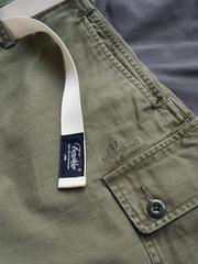 製品画像
ヴィンテージ感漂うバティック染めが特徴の多ポケットロングパンツ全体画像。ミリタリーテイストを取り入れ、300gのコットンサテン生地で耐久性と実用性を兼ね備えたデザイン。
詳細画像
バティック染めによる独特なテクスチャーや、取り外し可能なナイロンベルト、UTX Duraflexバックル、そして膝部分の補強パッチとYKK製カスタムジッパーのディテールショット。高い機能性が際立つ細部。