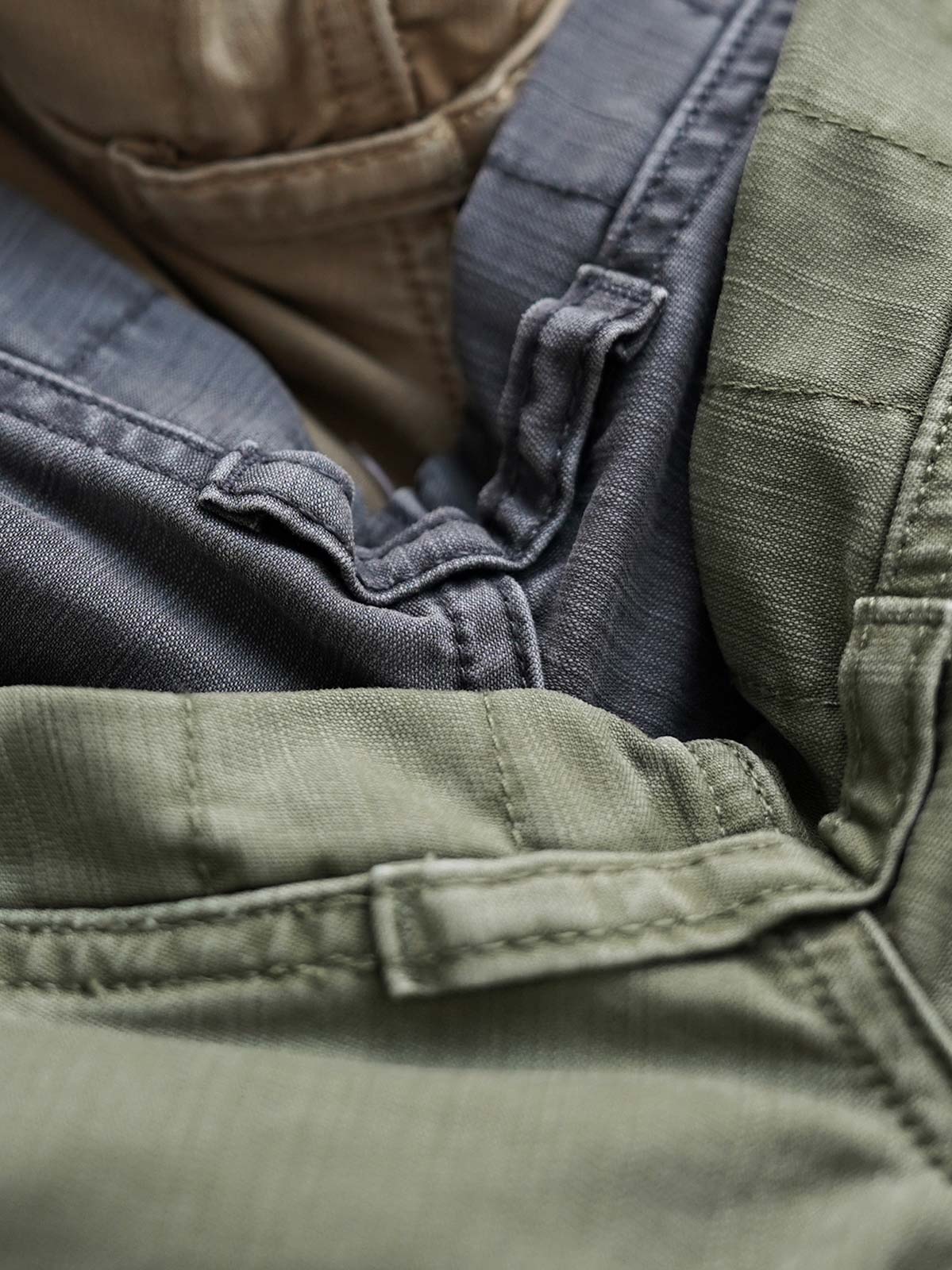 製品画像
ヴィンテージ感漂うバティック染めが特徴の多ポケットロングパンツ全体画像。ミリタリーテイストを取り入れ、300gのコットンサテン生地で耐久性と実用性を兼ね備えたデザイン。
詳細画像
バティック染めによる独特なテクスチャーや、取り外し可能なナイロンベルト、UTX Duraflexバックル、そして膝部分の補強パッチとYKK製カスタムジッパーのディテールショット。高い機能性が際立つ細部。