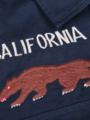 製品画像
厚手キャンバス生地で作られた刺繍キャンバスシャツの全体画像。1960年代のミリタリーユニフォームを再現したヴィンテージ感あるデザインが特徴。
詳細画像
フランス・ペリグーとアメリカ・カリフォルニア州をモチーフにした繊細な刺繍ディテールのクローズアップ。実用的なフラップ付きポケットも強調。