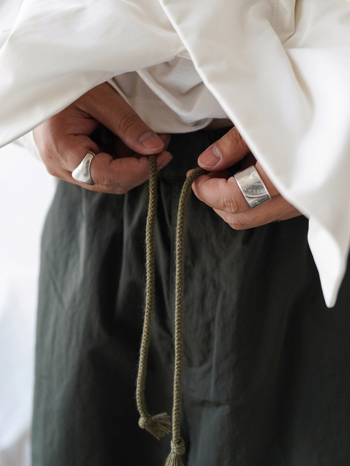 詳細画像
膝部分のダブルプリーツディテール、隠しポケット、UTX Duraflexドローコードエンド、そして反戦をテーマにしたデュポン紙ラベルのクローズアップ画像。機能性とディテールへのこだわりを強調。
モデル画像
シワ感テクスチャー素材のパラシュートパンツを着用したモデルが、機能性ジャケットと合わせたミリタリースタイルを披露。ワイドシルエットが快適さとトレンド感を演出。