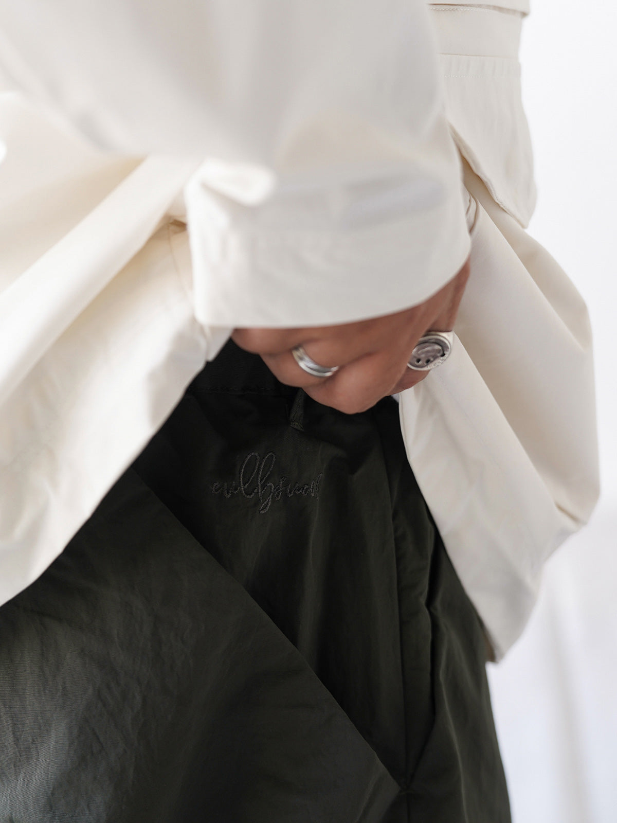 詳細画像
膝部分のダブルプリーツディテール、隠しポケット、UTX Duraflexドローコードエンド、そして反戦をテーマにしたデュポン紙ラベルのクローズアップ画像。機能性とディテールへのこだわりを強調。
モデル画像
シワ感テクスチャー素材のパラシュートパンツを着用したモデルが、機能性ジャケットと合わせたミリタリースタイルを披露。ワイドシルエットが快適さとトレンド感を演出。