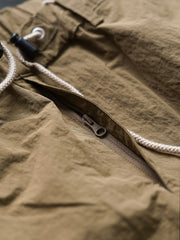 製品画像
撥水性に優れたナイロン素材を使用し、シワ感テクスチャーが特徴のミリタリーパラシュートパンツ全体画像。ダブルプリーツと多機能ポケットを備えたクラシックなシルエットが際立つデザイン。
詳細画像
膝部分のダブルプリーツディテール、隠しポケット、UTX Duraflexドローコードエンド、そして反戦をテーマにしたデュポン紙ラベルのクローズアップ画像。機能性とディテールへのこだわりを強調。