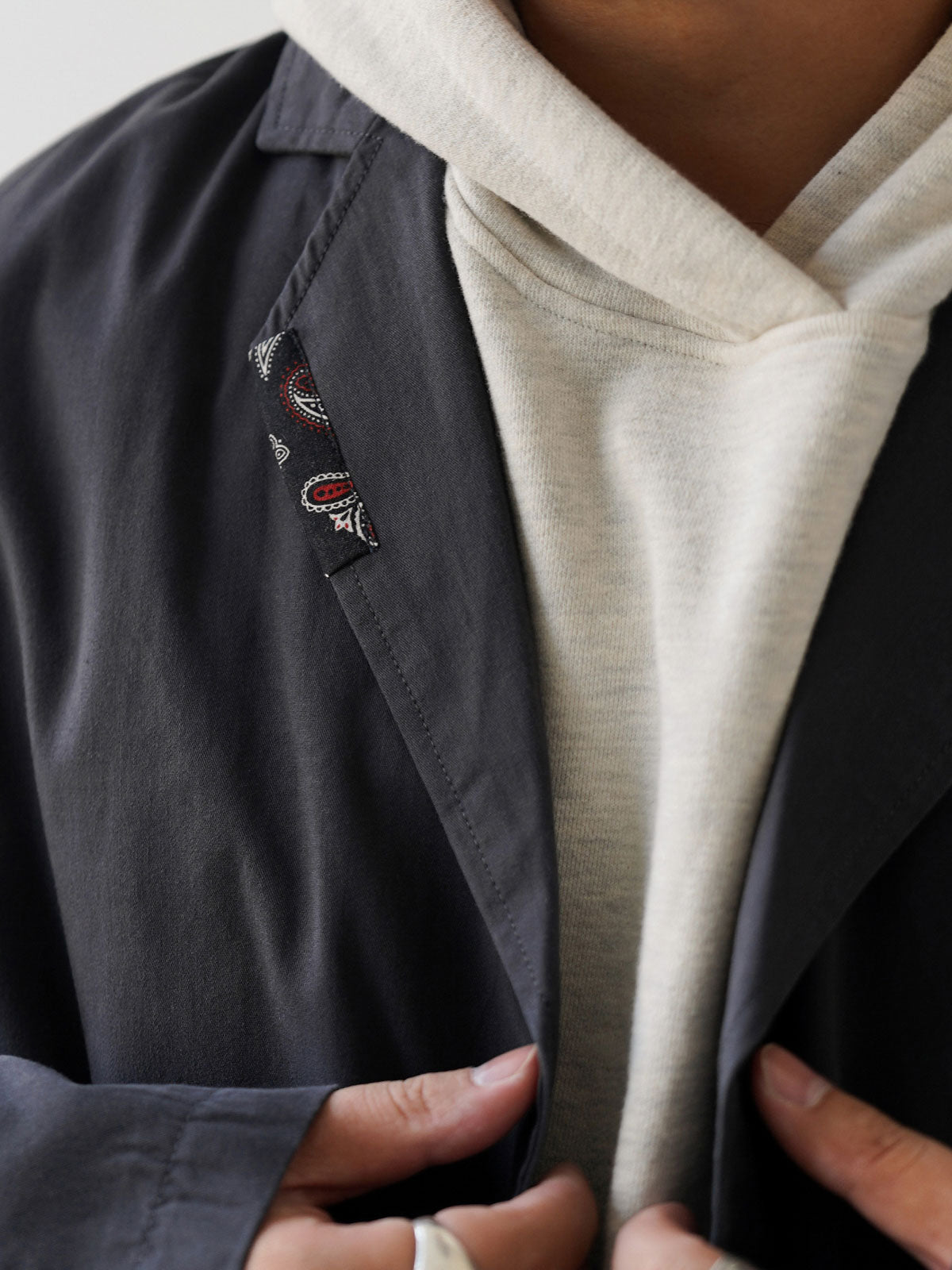 詳細画像
肩周りをすっきり見せるラグランスリーブデザインと、縫製部分を補強した三本針ステッチのクローズアップ画像。厚手リブ仕様のディテールも確認可能。
モデル画像
オートミールグレーとネイビーのバイカラー配色パーカーを着用したモデルが、ジーンズと合わせたヴィンテージカジュアルスタイルを披露。ゆったりシルエットが印象的。