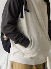 詳細画像
肩周りをすっきり見せるラグランスリーブデザインと、縫製部分を補強した三本針ステッチのクローズアップ画像。厚手リブ仕様のディテールも確認可能。
モデル画像
オートミールグレーとネイビーのバイカラー配色パーカーを着用したモデルが、ジーンズと合わせたヴィンテージカジュアルスタイルを披露。ゆったりシルエットが印象的。