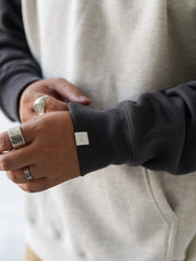 詳細画像
肩周りをすっきり見せるラグランスリーブデザインと、縫製部分を補強した三本針ステッチのクローズアップ画像。厚手リブ仕様のディテールも確認可能。
モデル画像
オートミールグレーとネイビーのバイカラー配色パーカーを着用したモデルが、ジーンズと合わせたヴィンテージカジュアルスタイルを披露。ゆったりシルエットが印象的。