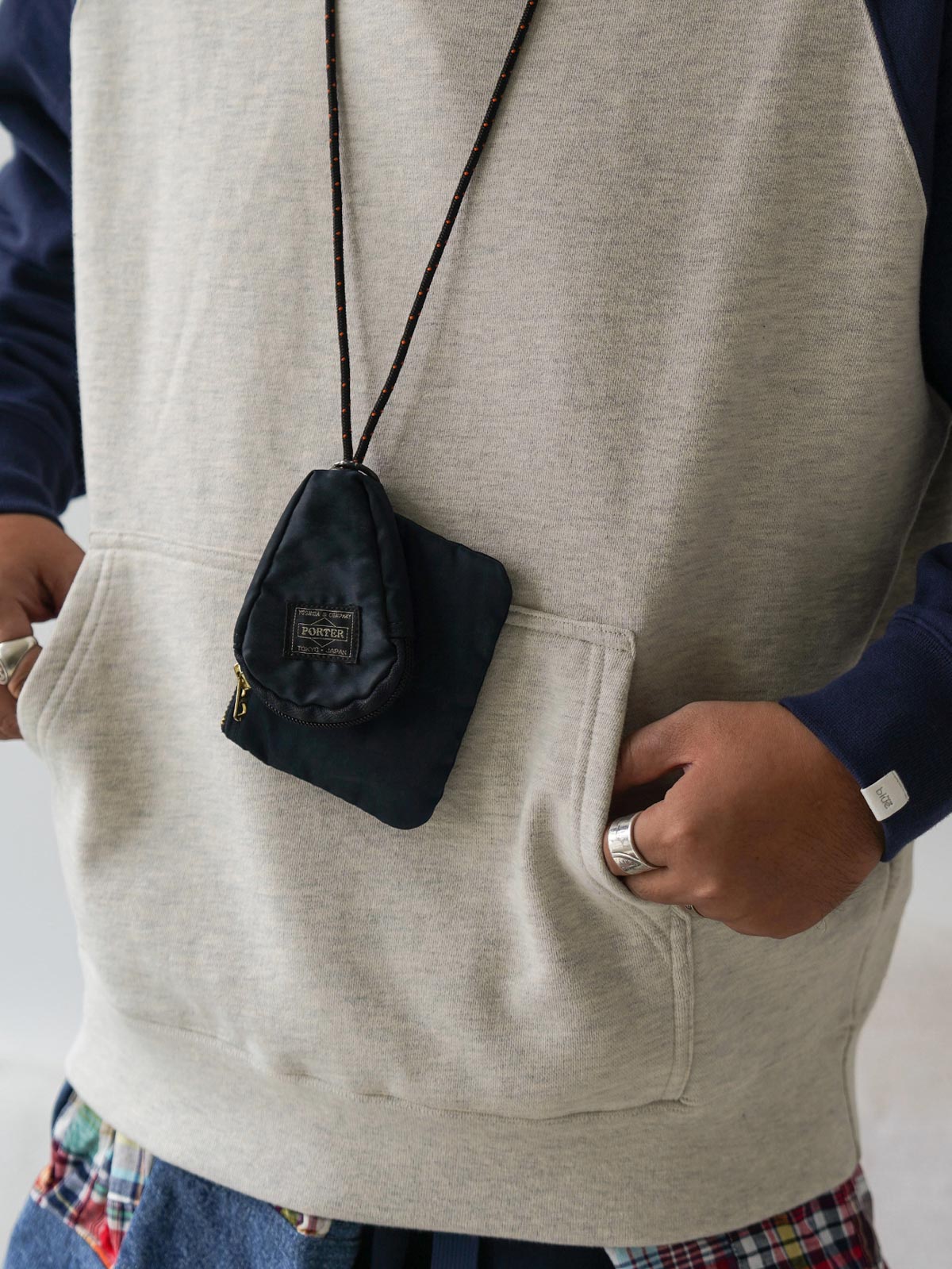 詳細画像
肩周りをすっきり見せるラグランスリーブデザインと、縫製部分を補強した三本針ステッチのクローズアップ画像。厚手リブ仕様のディテールも確認可能。
モデル画像
オートミールグレーとネイビーのバイカラー配色パーカーを着用したモデルが、ジーンズと合わせたヴィンテージカジュアルスタイルを披露。ゆったりシルエットが印象的。