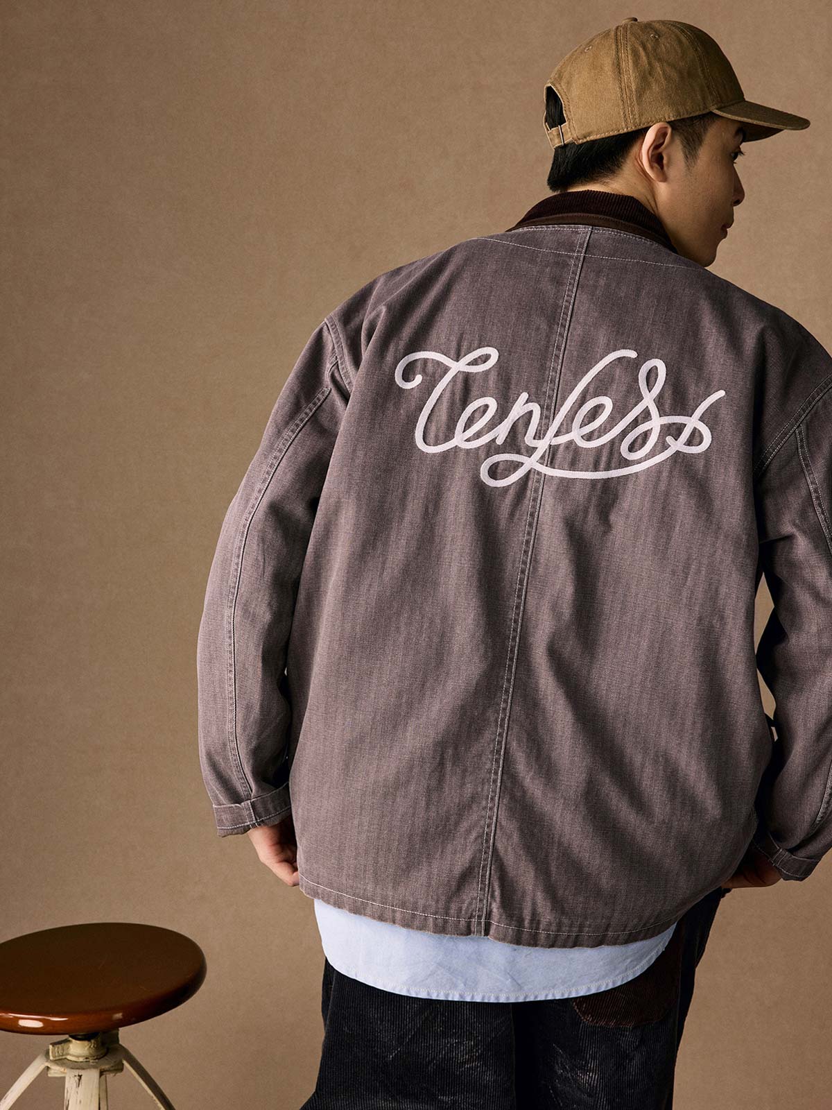 詳細画像
「ヘリンボーン生地のしっかりとしたテクスチャーとウォッシュ加工によるユーズド感、胸ポケットのラムウール織りディテールをクローズアップ。」
モデル画像
「インナーにシャツを合わせて着用したノーカラーフィッシングジャケット。ルーズフィットのシルエットがレイヤードスタイルを引き立てるヴィンテージ風コーディネート。」