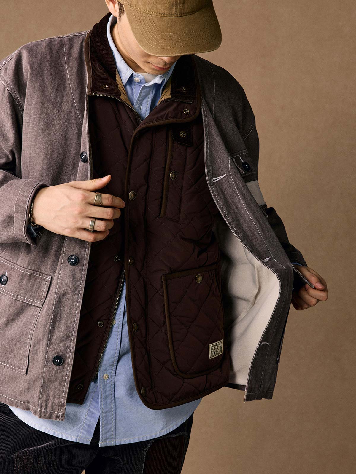 詳細画像
「ヘリンボーン生地のしっかりとしたテクスチャーとウォッシュ加工によるユーズド感、胸ポケットのラムウール織りディテールをクローズアップ。」
モデル画像
「インナーにシャツを合わせて着用したノーカラーフィッシングジャケット。ルーズフィットのシルエットがレイヤードスタイルを引き立てるヴィンテージ風コーディネート。」