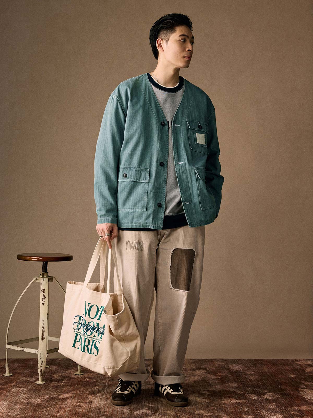 詳細画像
「ヘリンボーン生地のしっかりとしたテクスチャーとウォッシュ加工によるユーズド感、胸ポケットのラムウール織りディテールをクローズアップ。」
モデル画像
「インナーにシャツを合わせて着用したノーカラーフィッシングジャケット。ルーズフィットのシルエットがレイヤードスタイルを引き立てるヴィンテージ風コーディネート。」