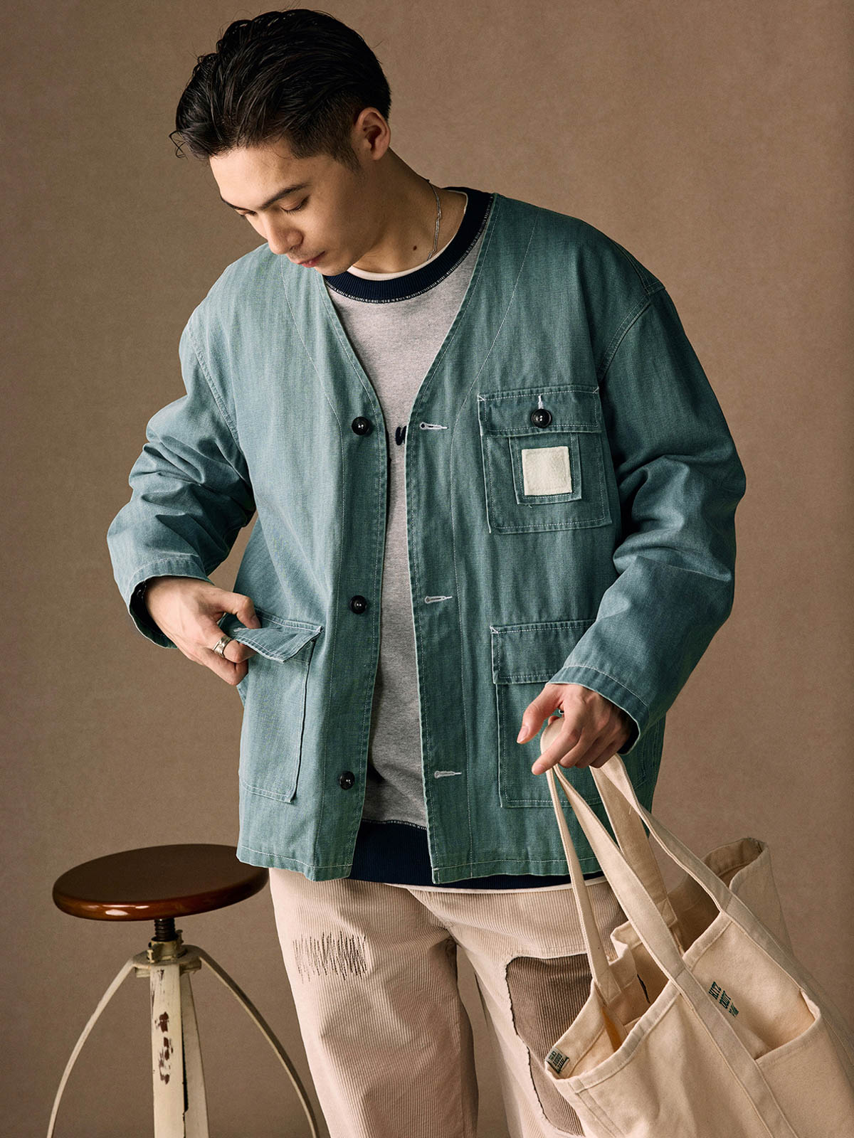 詳細画像
「ヘリンボーン生地のしっかりとしたテクスチャーとウォッシュ加工によるユーズド感、胸ポケットのラムウール織りディテールをクローズアップ。」
モデル画像
「インナーにシャツを合わせて着用したノーカラーフィッシングジャケット。ルーズフィットのシルエットがレイヤードスタイルを引き立てるヴィンテージ風コーディネート。」