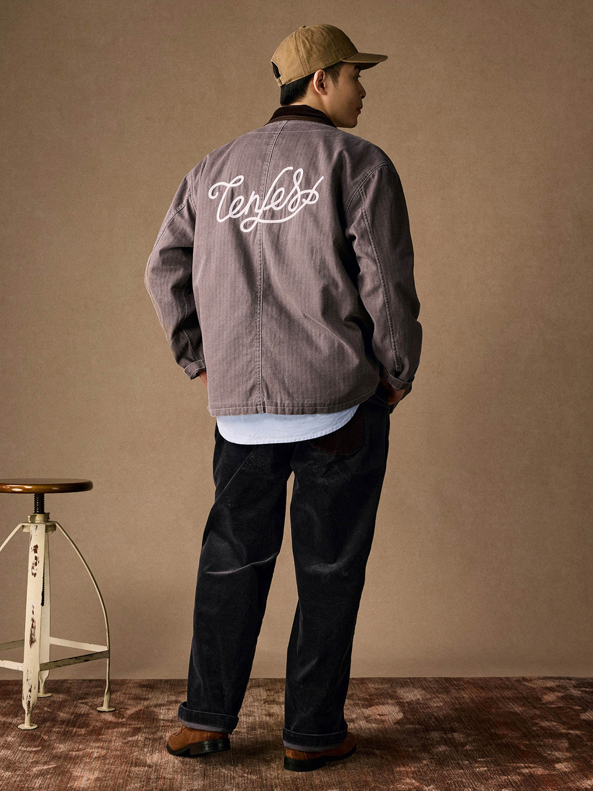 詳細画像
「ヘリンボーン生地のしっかりとしたテクスチャーとウォッシュ加工によるユーズド感、胸ポケットのラムウール織りディテールをクローズアップ。」
モデル画像
「インナーにシャツを合わせて着用したノーカラーフィッシングジャケット。ルーズフィットのシルエットがレイヤードスタイルを引き立てるヴィンテージ風コーディネート。」