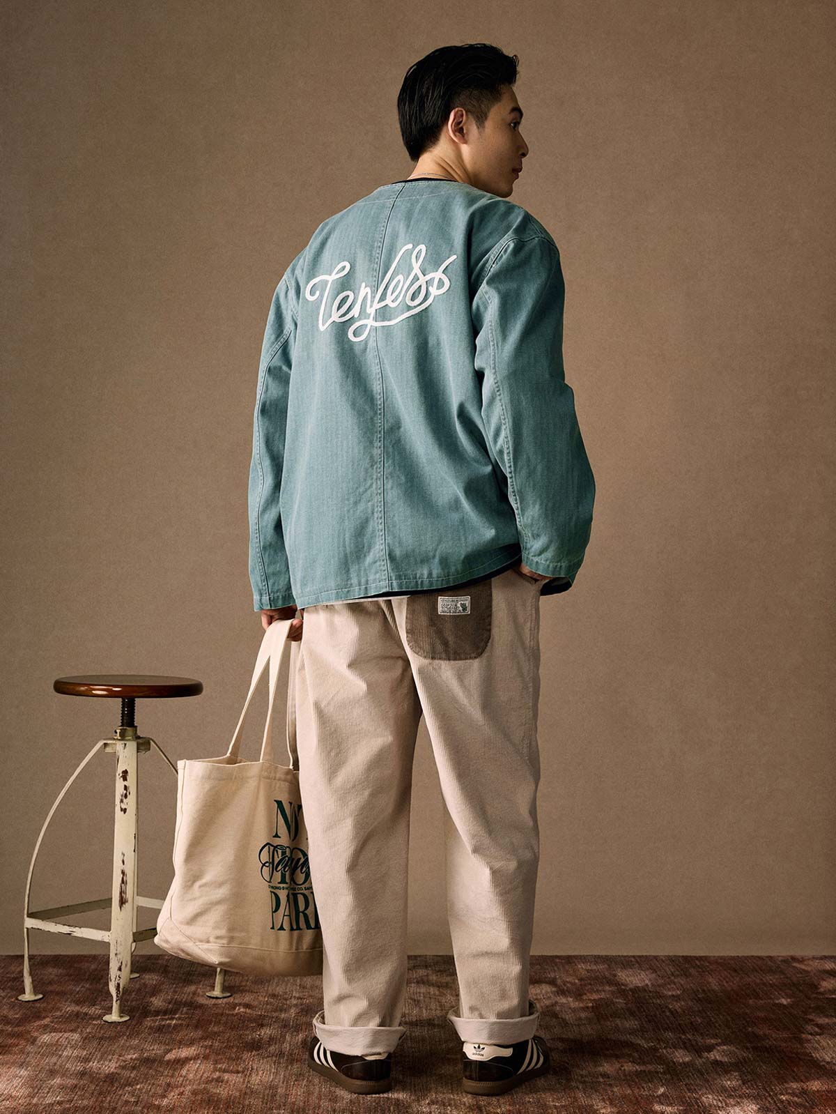 詳細画像
「ヘリンボーン生地のしっかりとしたテクスチャーとウォッシュ加工によるユーズド感、胸ポケットのラムウール織りディテールをクローズアップ。」
モデル画像
「インナーにシャツを合わせて着用したノーカラーフィッシングジャケット。ルーズフィットのシルエットがレイヤードスタイルを引き立てるヴィンテージ風コーディネート。」