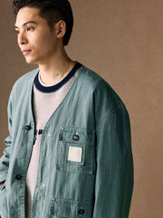 詳細画像
「ヘリンボーン生地のしっかりとしたテクスチャーとウォッシュ加工によるユーズド感、胸ポケットのラムウール織りディテールをクローズアップ。」
モデル画像
「インナーにシャツを合わせて着用したノーカラーフィッシングジャケット。ルーズフィットのシルエットがレイヤードスタイルを引き立てるヴィンテージ風コーディネート。」
