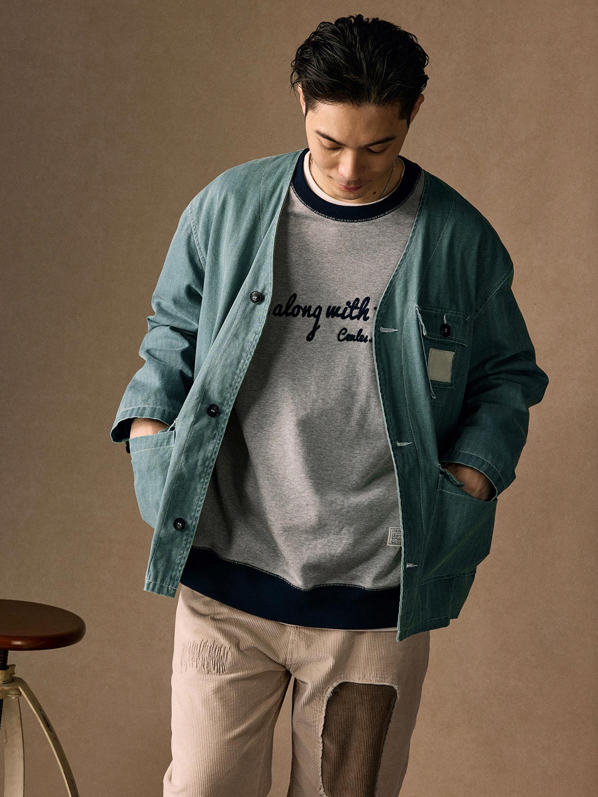 詳細画像
「ヘリンボーン生地のしっかりとしたテクスチャーとウォッシュ加工によるユーズド感、胸ポケットのラムウール織りディテールをクローズアップ。」
モデル画像
「インナーにシャツを合わせて着用したノーカラーフィッシングジャケット。ルーズフィットのシルエットがレイヤードスタイルを引き立てるヴィンテージ風コーディネート。」