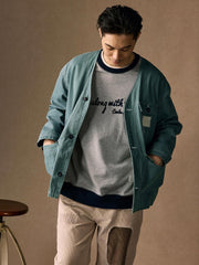 詳細画像
「ヘリンボーン生地のしっかりとしたテクスチャーとウォッシュ加工によるユーズド感、胸ポケットのラムウール織りディテールをクローズアップ。」
モデル画像
「インナーにシャツを合わせて着用したノーカラーフィッシングジャケット。ルーズフィットのシルエットがレイヤードスタイルを引き立てるヴィンテージ風コーディネート。」