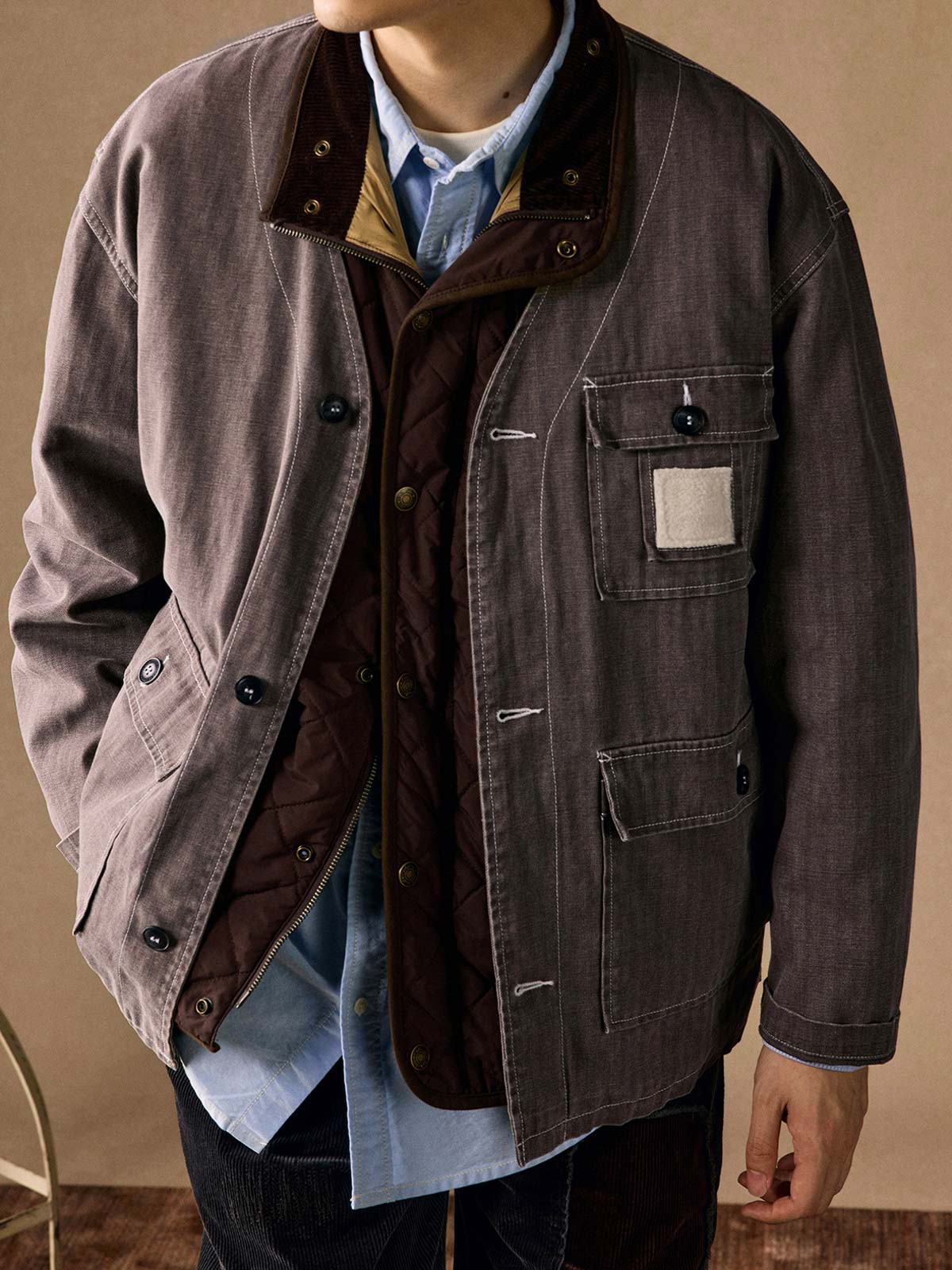 詳細画像
「ヘリンボーン生地のしっかりとしたテクスチャーとウォッシュ加工によるユーズド感、胸ポケットのラムウール織りディテールをクローズアップ。」
モデル画像
「インナーにシャツを合わせて着用したノーカラーフィッシングジャケット。ルーズフィットのシルエットがレイヤードスタイルを引き立てるヴィンテージ風コーディネート。」