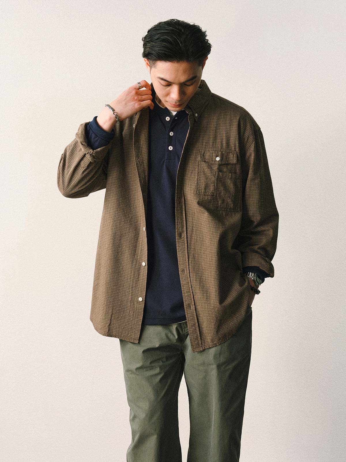 詳細画像
「胸元のユニークな配置のパッチポケットと立体感のあるチェック柄生地のディテールをクローズアップ。シワになりにくい特性も備えた高品質なコットン素材。」
モデル画像
「モデルがネイビーのチェック柄パッチポケットシャツを着用し、デニムパンツと合わせたカジュアルなコーディネートを披露。」