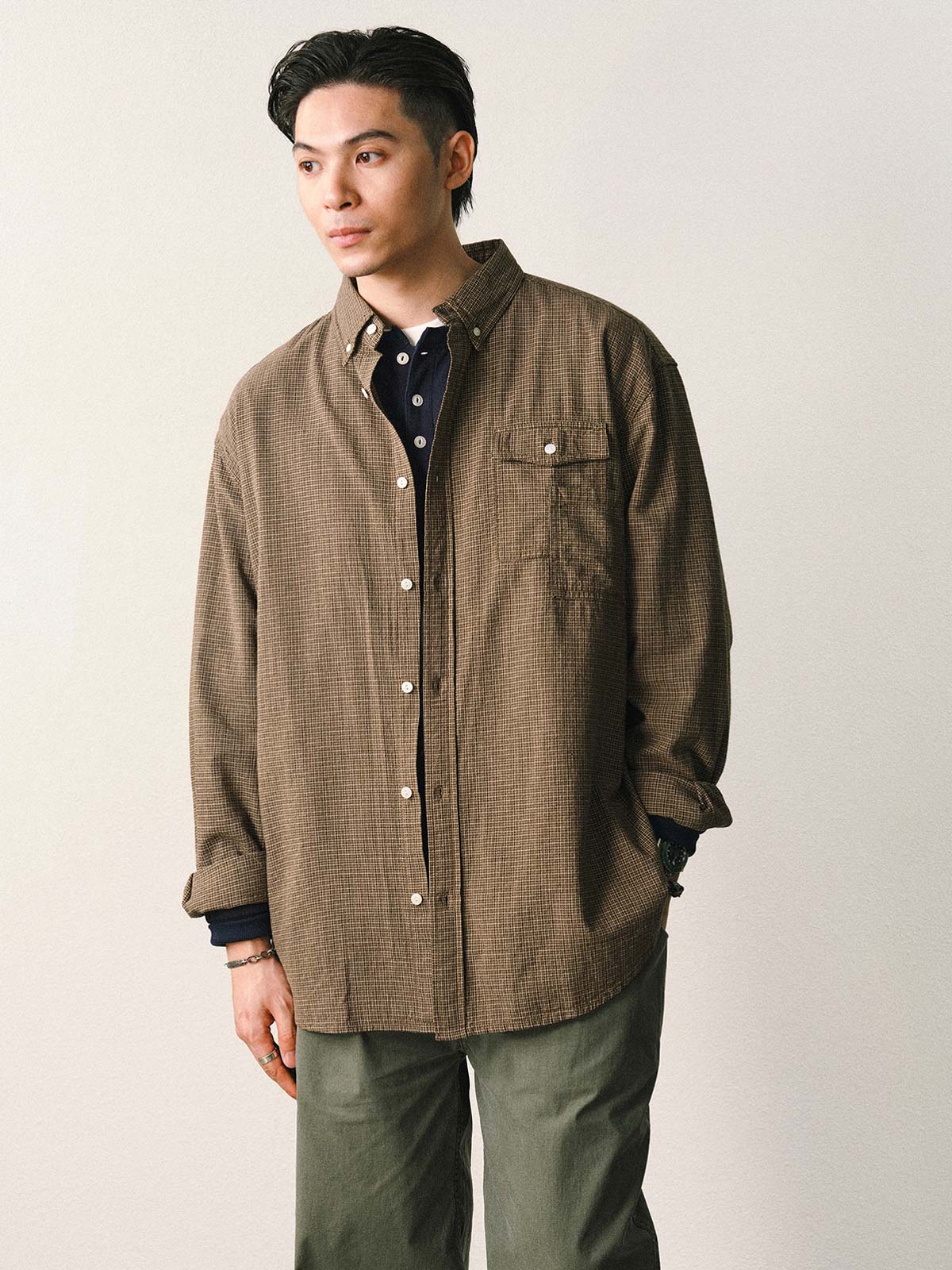 詳細画像
「胸元のユニークな配置のパッチポケットと立体感のあるチェック柄生地のディテールをクローズアップ。シワになりにくい特性も備えた高品質なコットン素材。」
モデル画像
「モデルがネイビーのチェック柄パッチポケットシャツを着用し、デニムパンツと合わせたカジュアルなコーディネートを披露。」