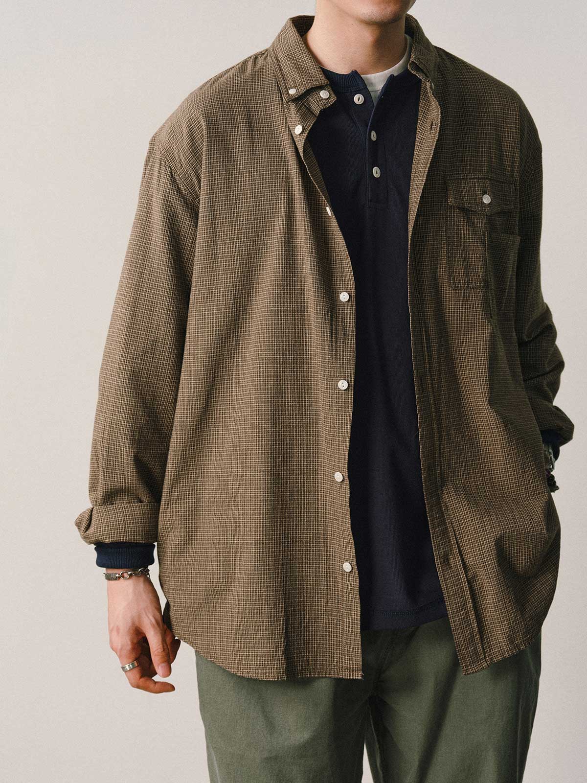 詳細画像
「胸元のユニークな配置のパッチポケットと立体感のあるチェック柄生地のディテールをクローズアップ。シワになりにくい特性も備えた高品質なコットン素材。」
モデル画像
「モデルがネイビーのチェック柄パッチポケットシャツを着用し、デニムパンツと合わせたカジュアルなコーディネートを披露。」