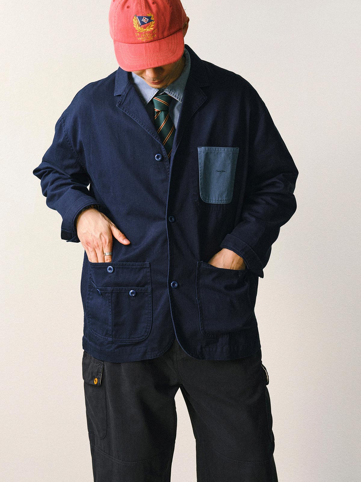 詳細画像
「バイカラーの胸ポケットやアシンメトリーな複合ポケットのディテールクローズアップ。酵素ウォッシュ加工による自然な色褪せ感と軽い起毛感が特徴。」
モデル画像
「モデルがアーミーグリーンのウォッシュ加工ワークテイストテーラードジャケットをデニムと合わせたヴィンテージ風カジュアルワークコーディネート。」