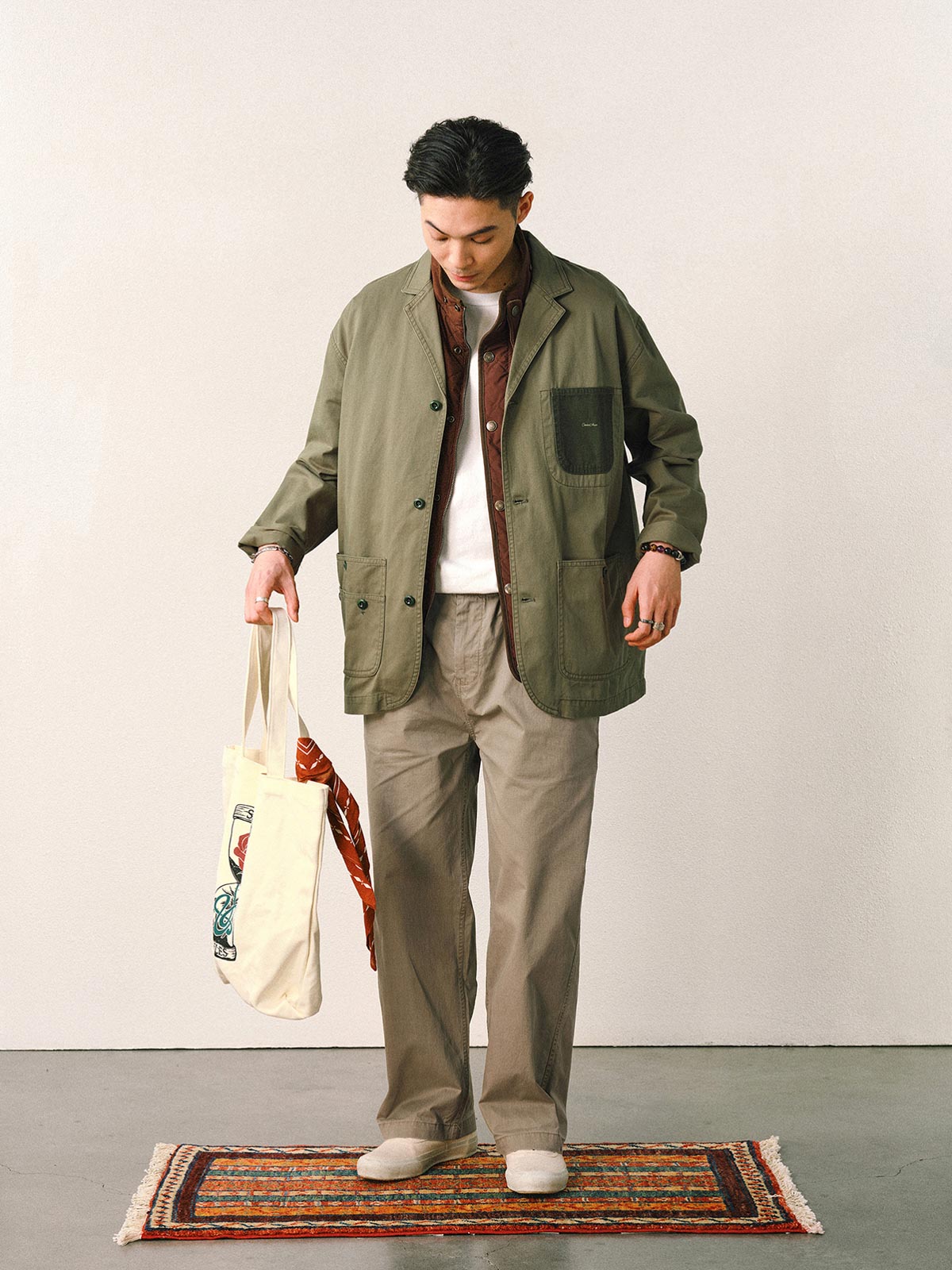 詳細画像
「バイカラーの胸ポケットやアシンメトリーな複合ポケットのディテールクローズアップ。酵素ウォッシュ加工による自然な色褪せ感と軽い起毛感が特徴。」
モデル画像
「モデルがアーミーグリーンのウォッシュ加工ワークテイストテーラードジャケットをデニムと合わせたヴィンテージ風カジュアルワークコーディネート。」