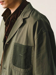 詳細画像
「バイカラーの胸ポケットやアシンメトリーな複合ポケットのディテールクローズアップ。酵素ウォッシュ加工による自然な色褪せ感と軽い起毛感が特徴。」
モデル画像
「モデルがアーミーグリーンのウォッシュ加工ワークテイストテーラードジャケットをデニムと合わせたヴィンテージ風カジュアルワークコーディネート。」