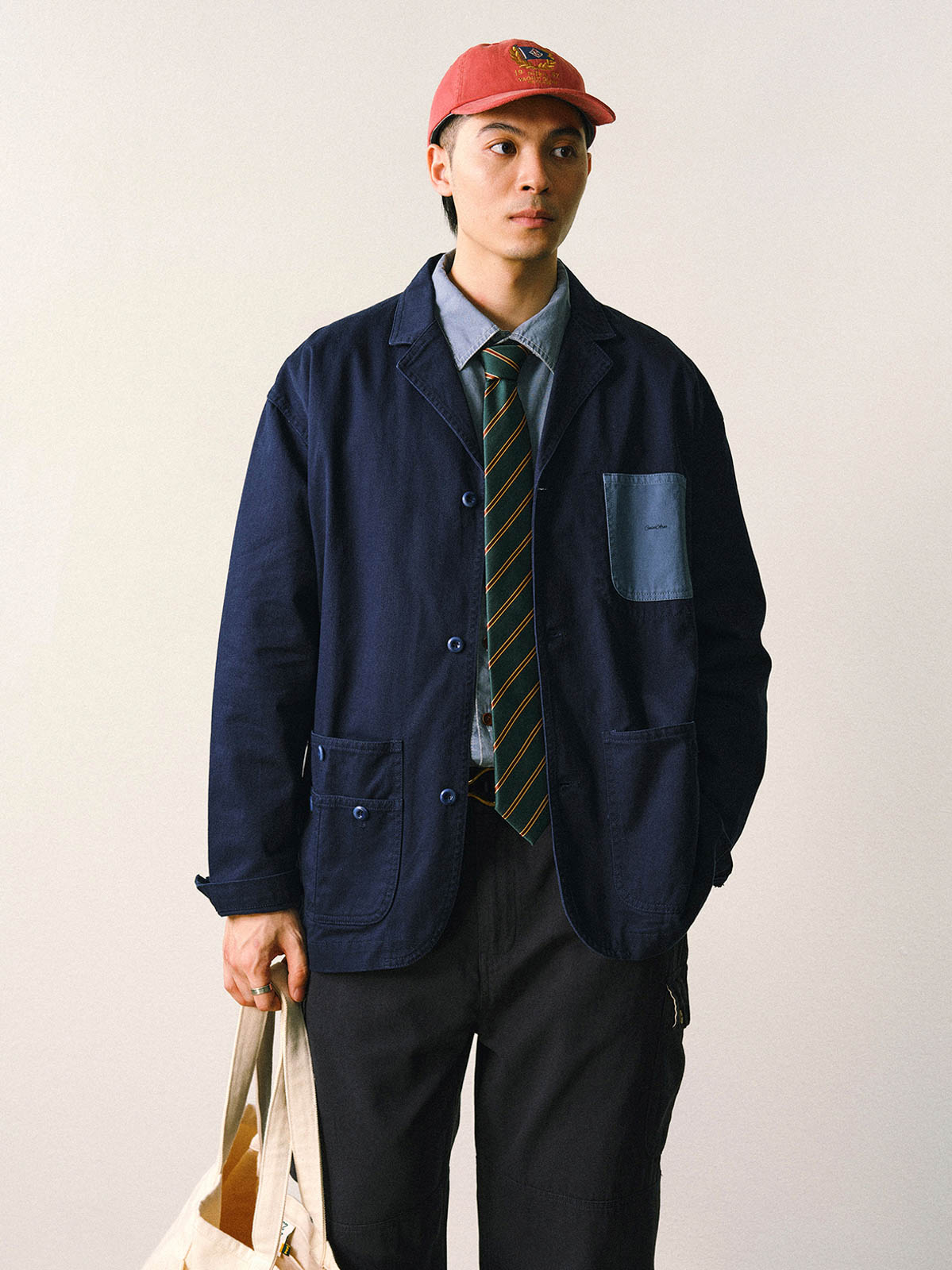 詳細画像
「バイカラーの胸ポケットやアシンメトリーな複合ポケットのディテールクローズアップ。酵素ウォッシュ加工による自然な色褪せ感と軽い起毛感が特徴。」
モデル画像
「モデルがアーミーグリーンのウォッシュ加工ワークテイストテーラードジャケットをデニムと合わせたヴィンテージ風カジュアルワークコーディネート。」