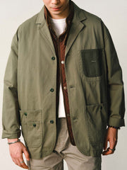 詳細画像
「バイカラーの胸ポケットやアシンメトリーな複合ポケットのディテールクローズアップ。酵素ウォッシュ加工による自然な色褪せ感と軽い起毛感が特徴。」
モデル画像
「モデルがアーミーグリーンのウォッシュ加工ワークテイストテーラードジャケットをデニムと合わせたヴィンテージ風カジュアルワークコーディネート。」