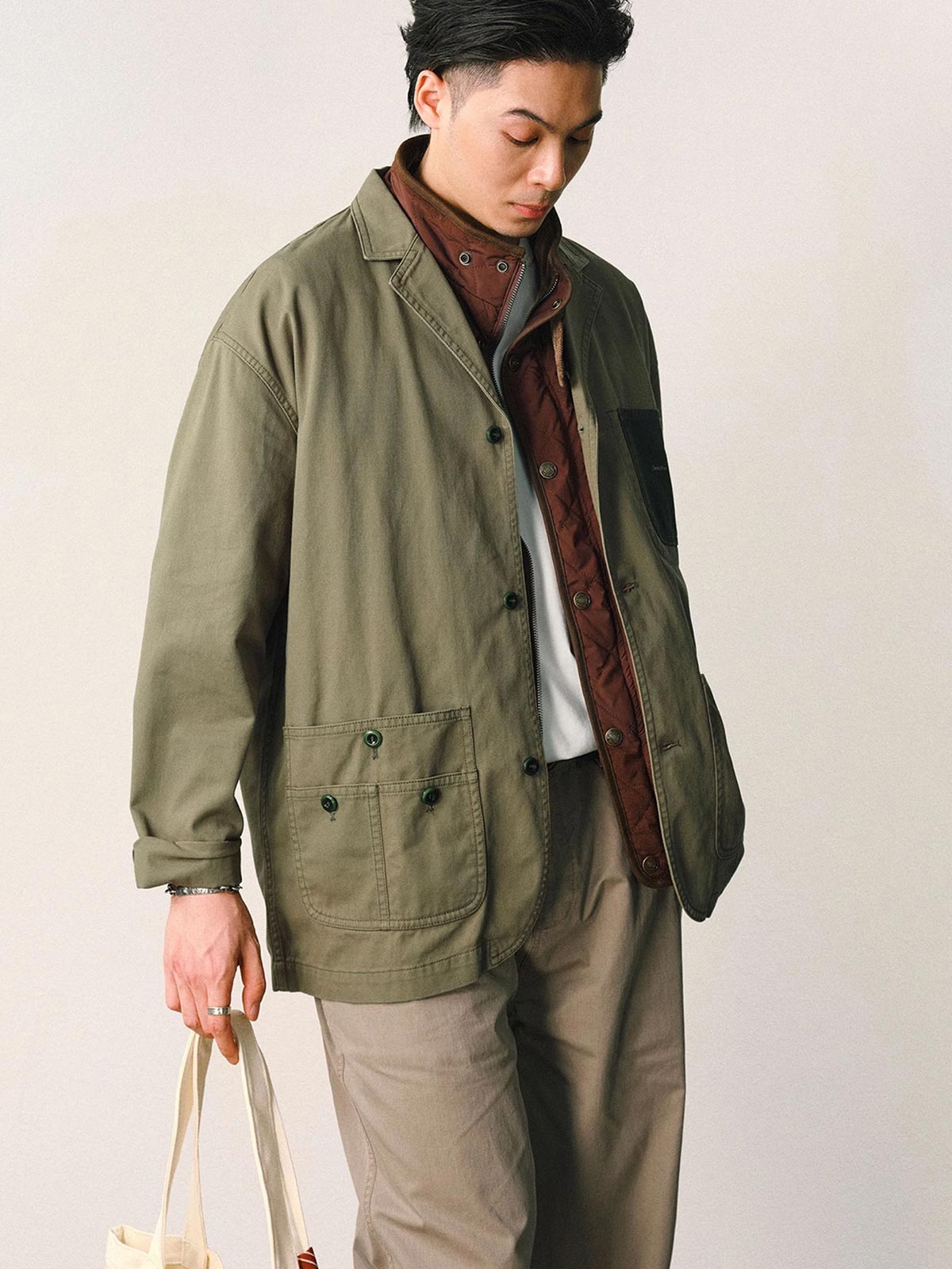 詳細画像
「バイカラーの胸ポケットやアシンメトリーな複合ポケットのディテールクローズアップ。酵素ウォッシュ加工による自然な色褪せ感と軽い起毛感が特徴。」
モデル画像
「モデルがアーミーグリーンのウォッシュ加工ワークテイストテーラードジャケットをデニムと合わせたヴィンテージ風カジュアルワークコーディネート。」