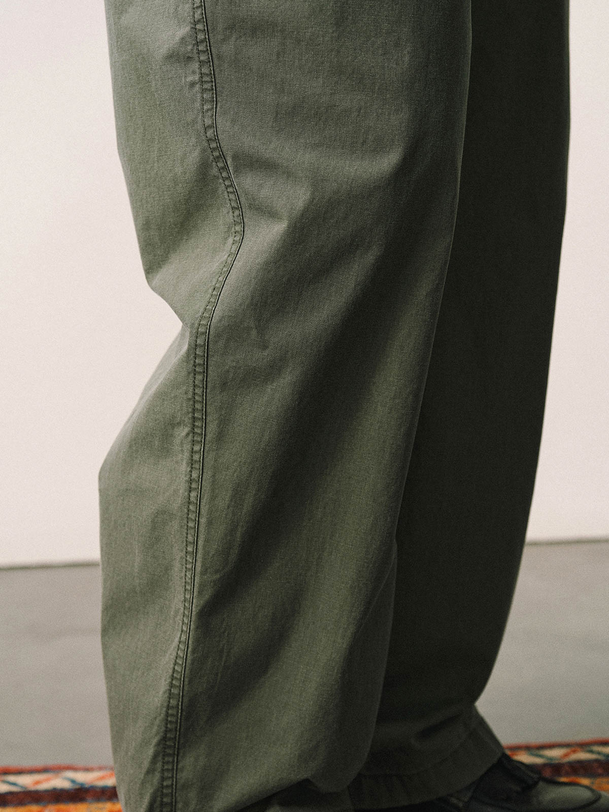 詳細画像
「スラブツイルの竹節模様とヘリンボーンパターンの切り替えデザインをクローズアップ。自然な色褪せ感とパイピング仕上げが高級感を引き立てるディテール。」
モデル画像
「モデルが白シャツとスニーカーを合わせて着用したカーキのヴィンテージ加工スラブ織りテクスチャーパンツのコーディネート。」