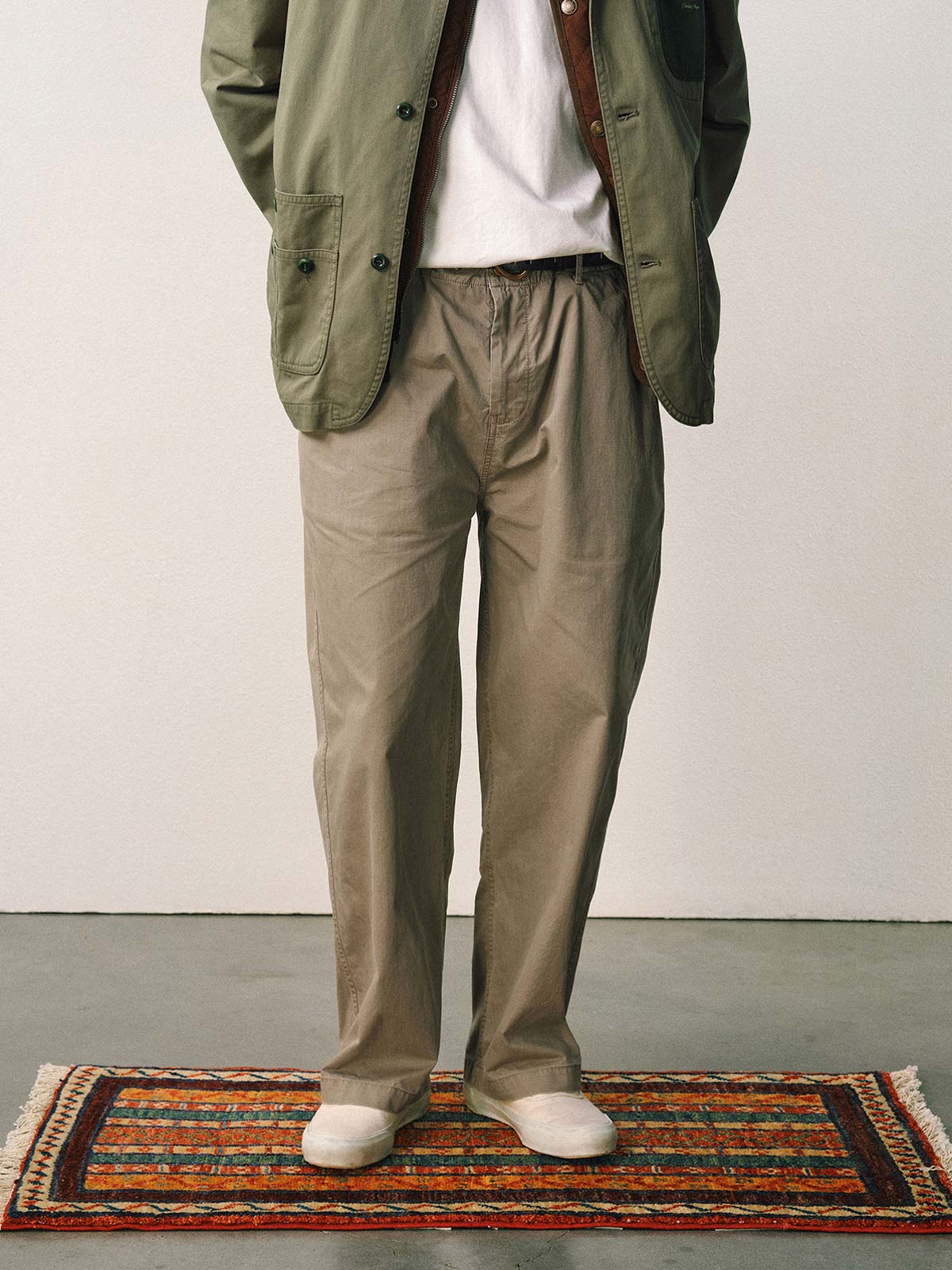 詳細画像
「スラブツイルの竹節模様とヘリンボーンパターンの切り替えデザインをクローズアップ。自然な色褪せ感とパイピング仕上げが高級感を引き立てるディテール。」
モデル画像
「モデルが白シャツとスニーカーを合わせて着用したカーキのヴィンテージ加工スラブ織りテクスチャーパンツのコーディネート。」