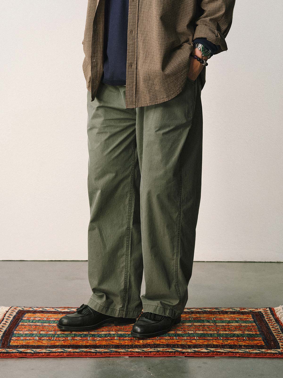 詳細画像
「スラブツイルの竹節模様とヘリンボーンパターンの切り替えデザインをクローズアップ。自然な色褪せ感とパイピング仕上げが高級感を引き立てるディテール。」
モデル画像
「モデルが白シャツとスニーカーを合わせて着用したカーキのヴィンテージ加工スラブ織りテクスチャーパンツのコーディネート。」