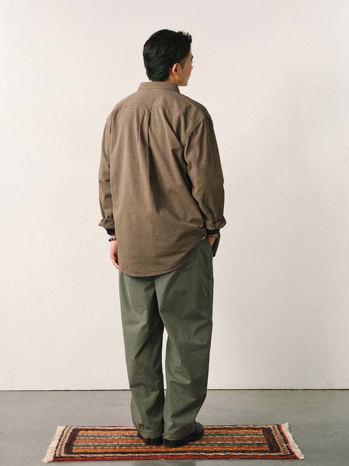 詳細画像
「スラブツイルの竹節模様とヘリンボーンパターンの切り替えデザインをクローズアップ。自然な色褪せ感とパイピング仕上げが高級感を引き立てるディテール。」
モデル画像
「モデルが白シャツとスニーカーを合わせて着用したカーキのヴィンテージ加工スラブ織りテクスチャーパンツのコーディネート。」