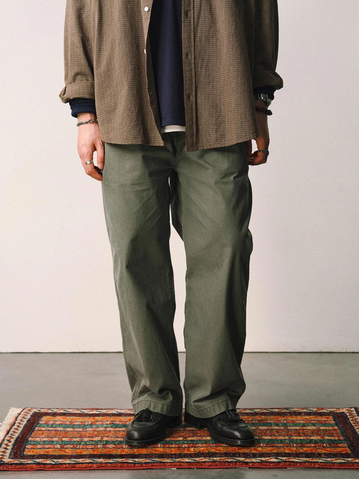 詳細画像
「スラブツイルの竹節模様とヘリンボーンパターンの切り替えデザインをクローズアップ。自然な色褪せ感とパイピング仕上げが高級感を引き立てるディテール。」
モデル画像
「モデルが白シャツとスニーカーを合わせて着用したカーキのヴィンテージ加工スラブ織りテクスチャーパンツのコーディネート。」